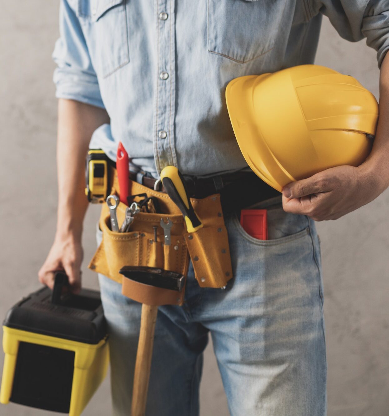 Worker man holding construction helmet and toolbox near wall. Male hand tools for house renovation